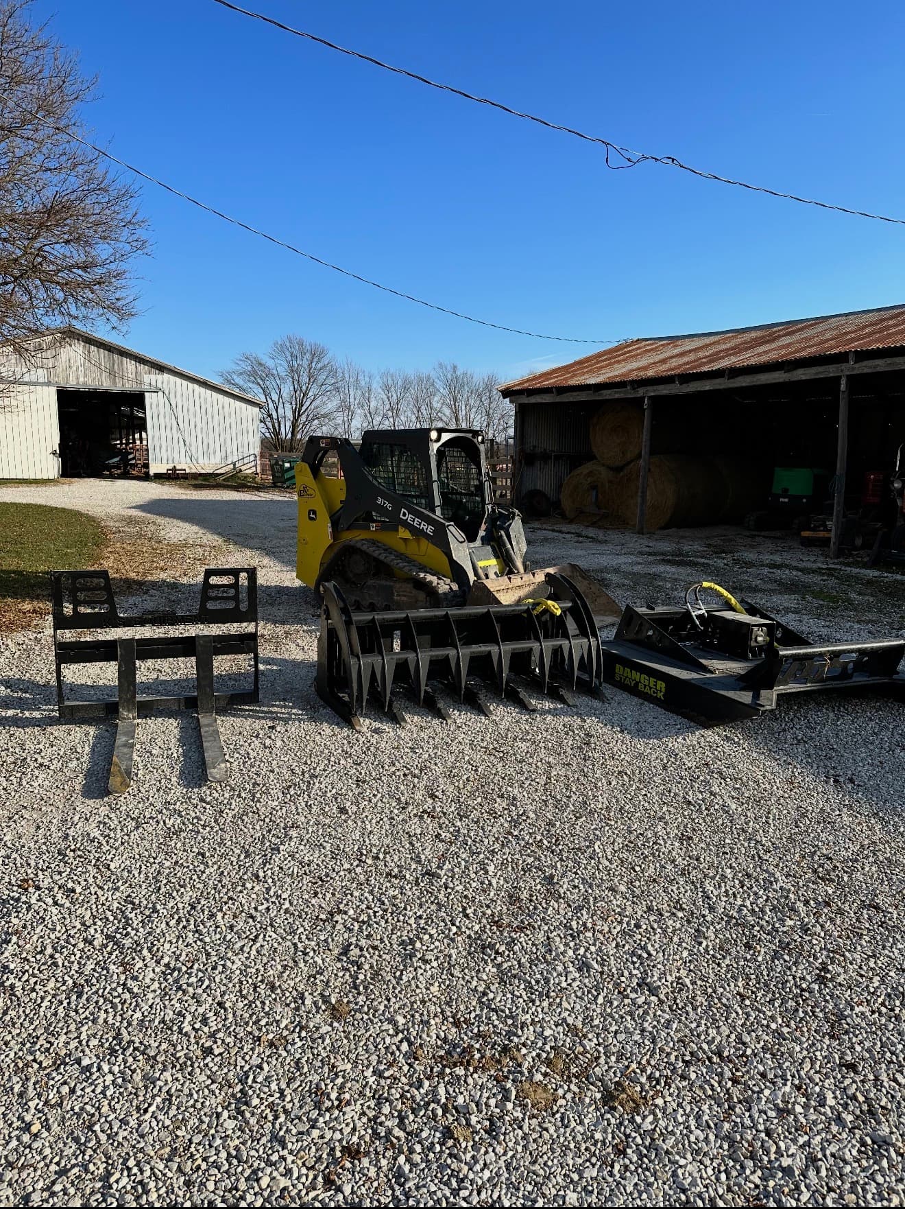 All five skid steer attachments laid out — brush cutter, forks, grapple, tooth bucket, smooth bucket